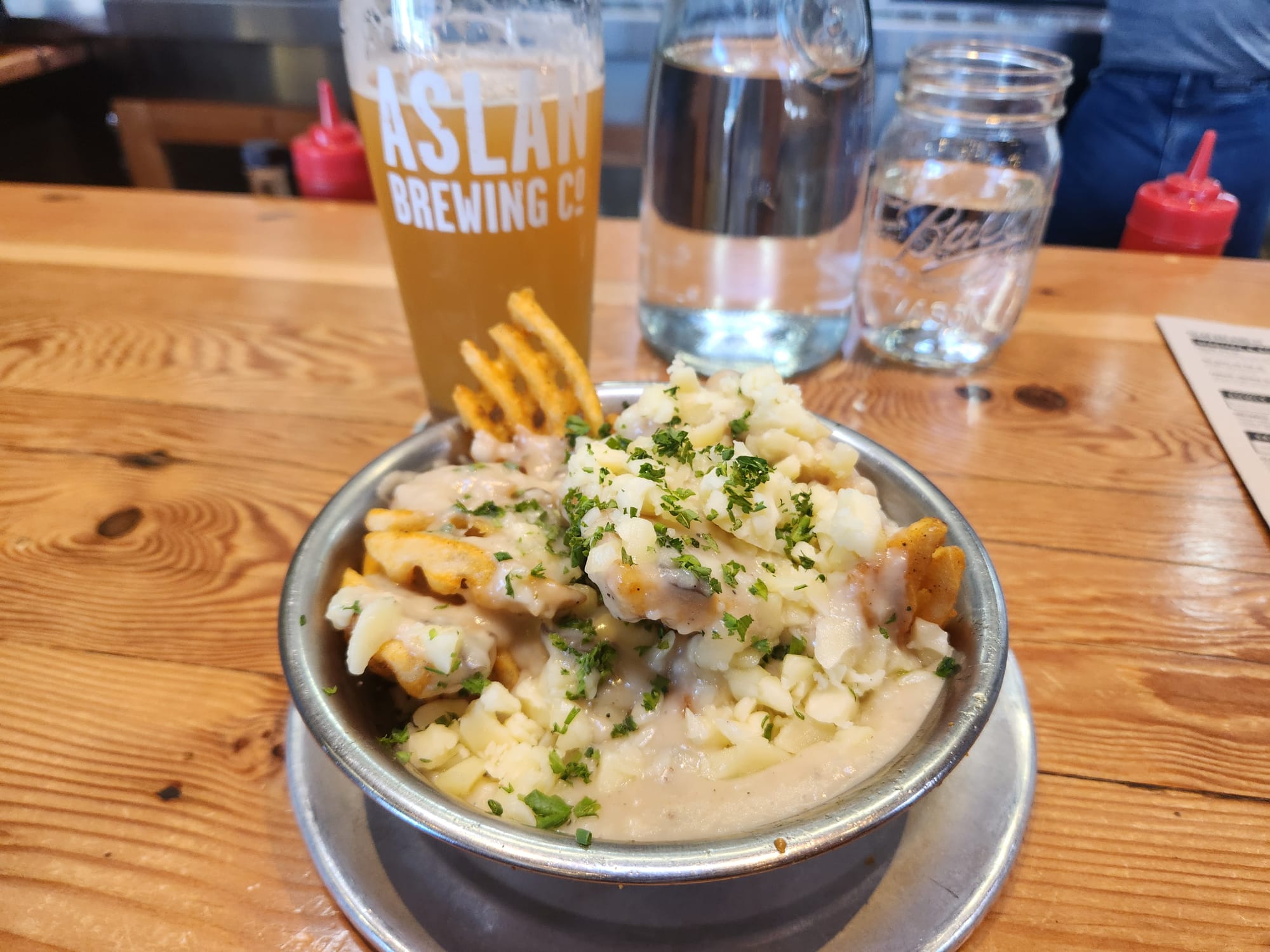 A bowl of poutine with plenty of gravy and cheese curds, with a pint of beer from Aslan Brewing Co. 