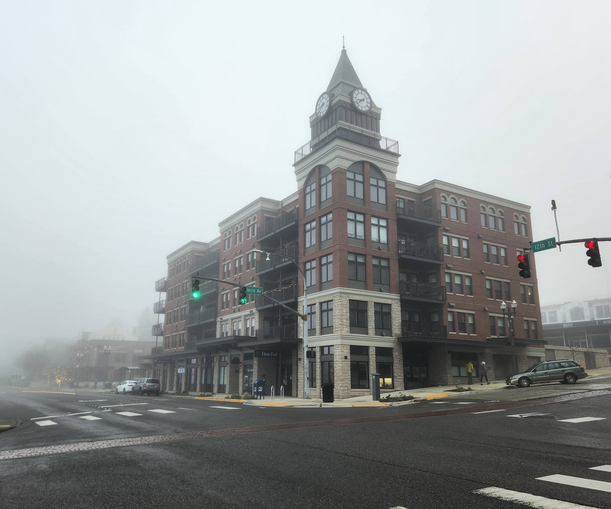 A 5-story red brick building with a corner clocktower surrounded by fog. 