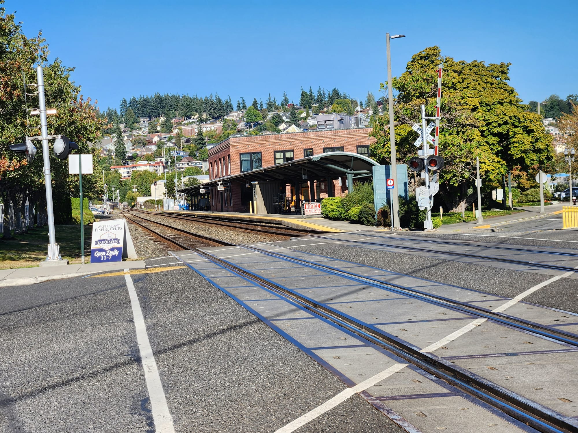 Two railroad tracks cut across a street and serve an adjacent train platform at a red brick station.