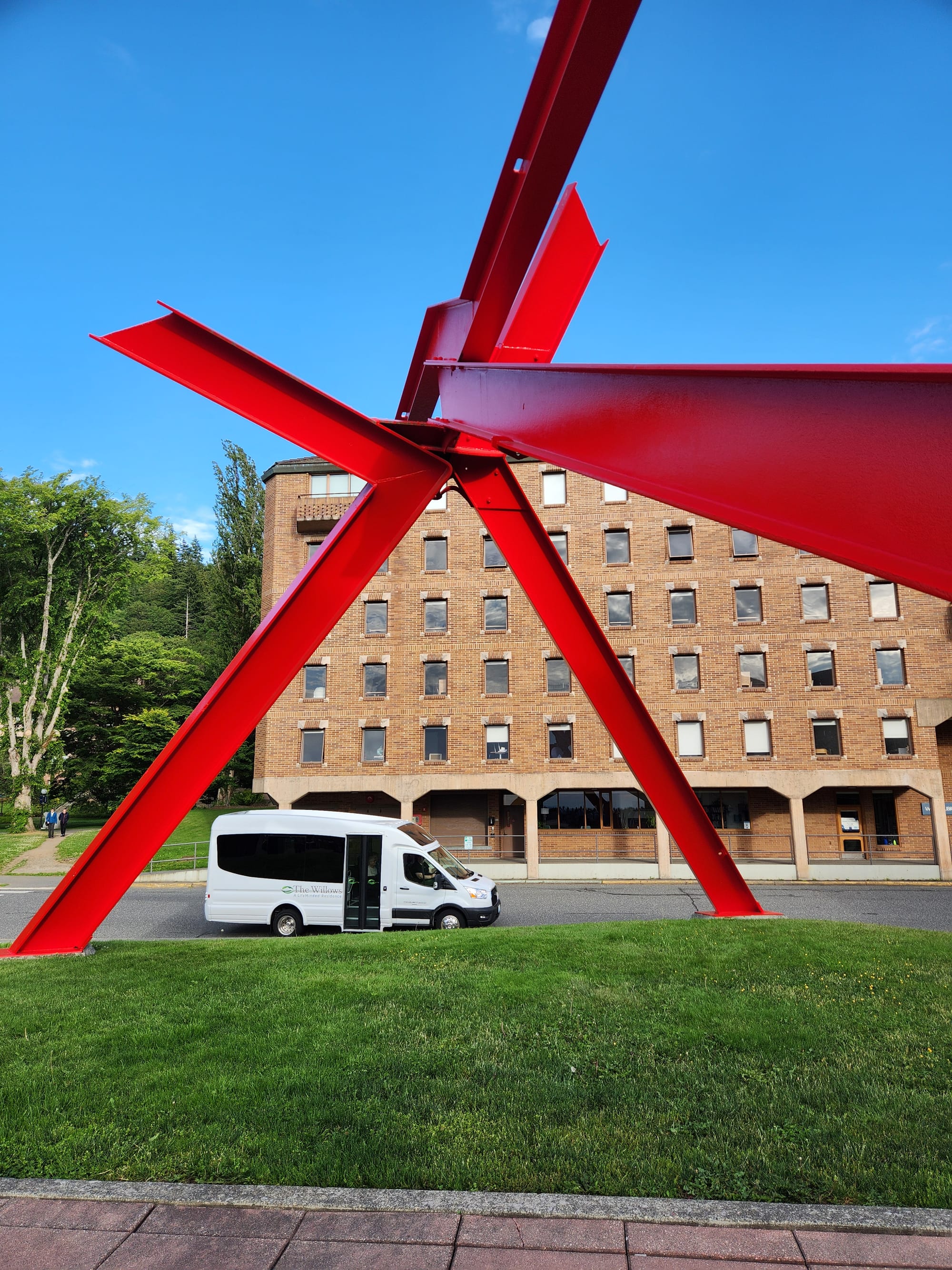 A white shuttle van on a street adjacent to a bright red outdoor sculture.