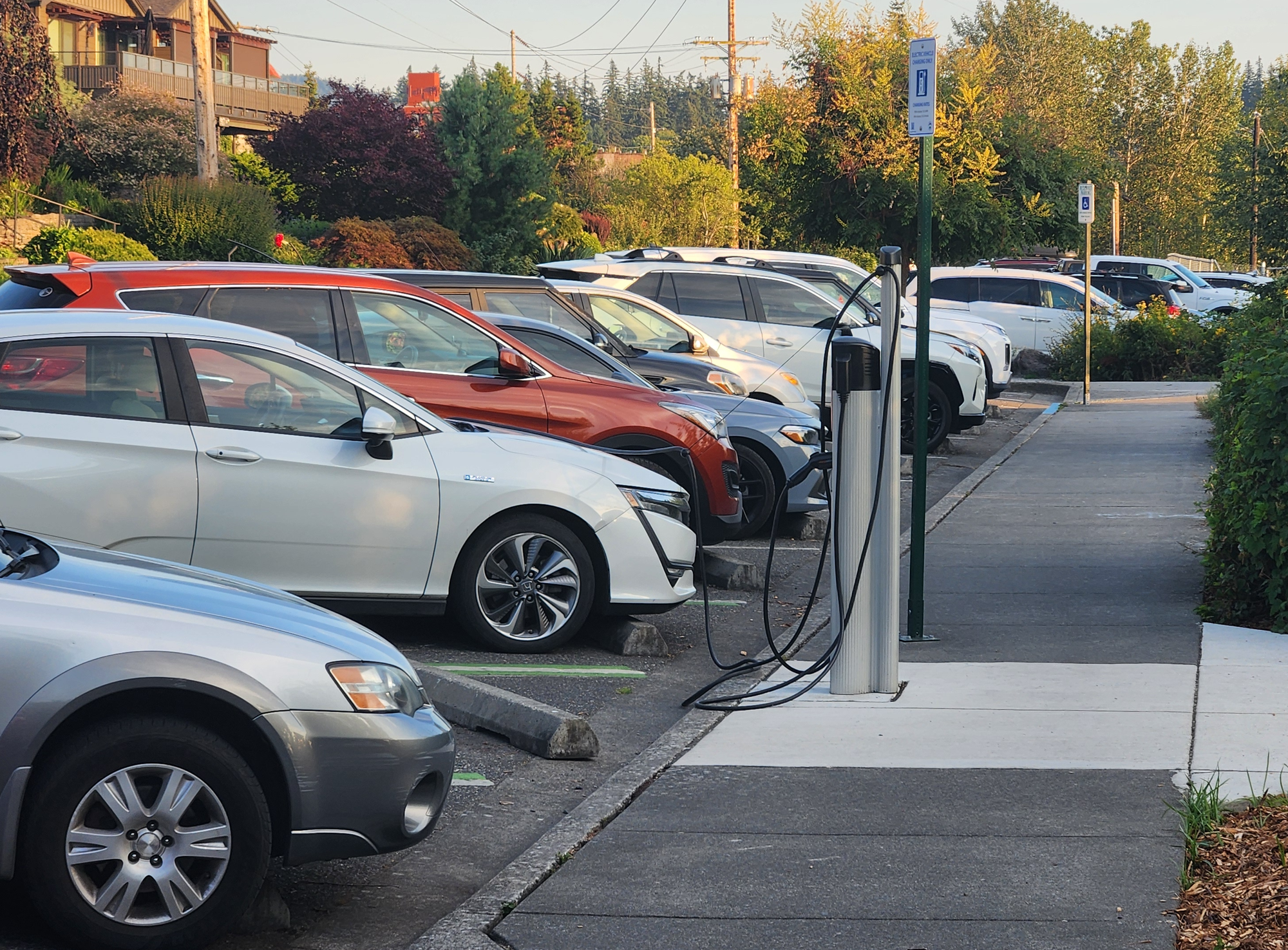 Cars, SUVs and trucks parked in angled parking spaces, including an electric plug-in vehicle at a charging station.