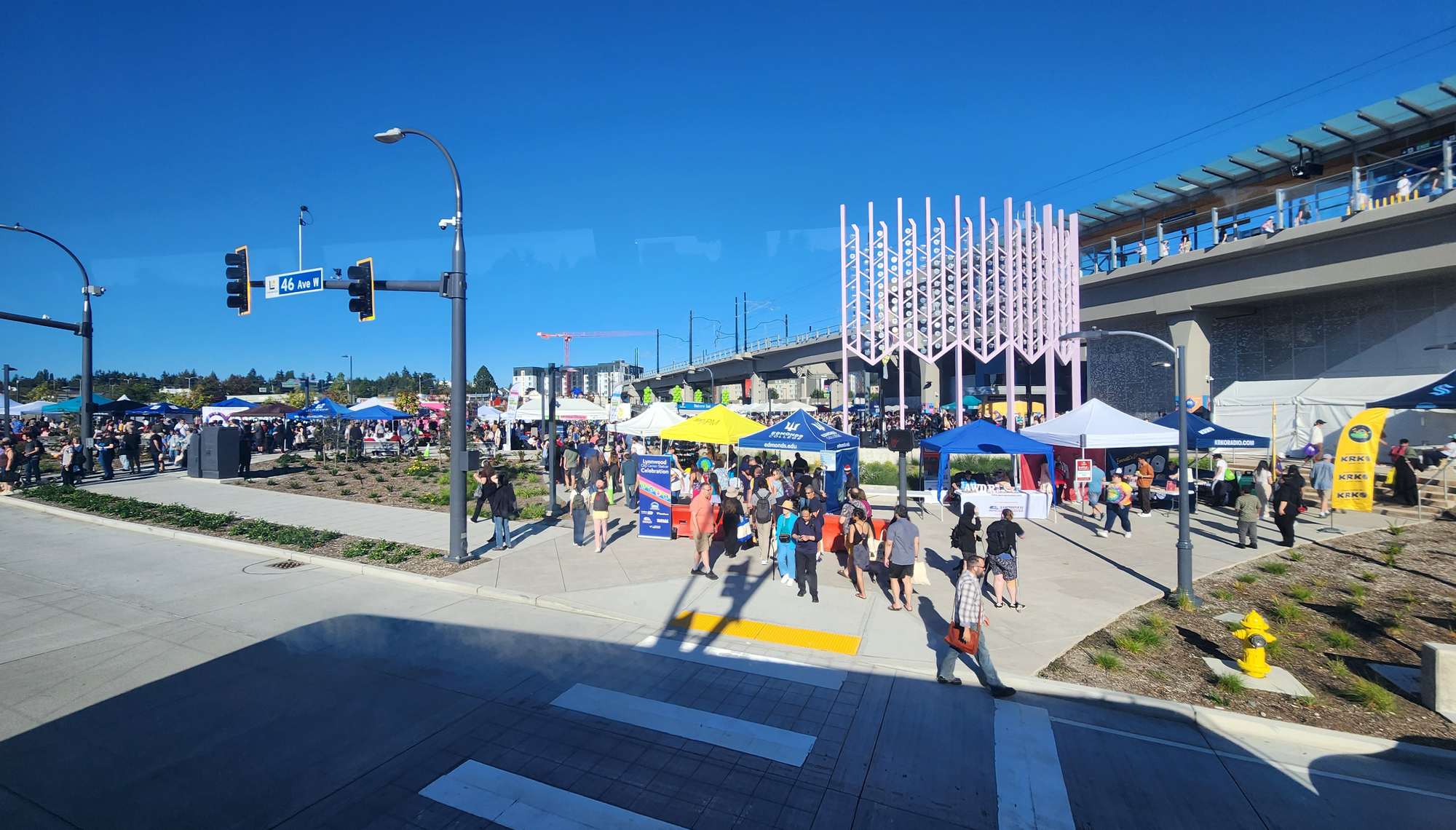 An elevated rail station with public art on the plaza, which is hosting a community celebration.