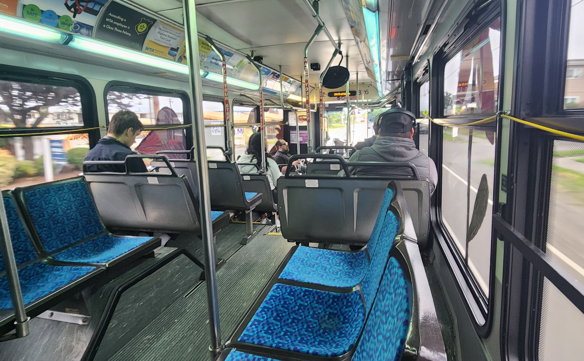 An interior photo of a bus with blue seats and a dozen passengers.