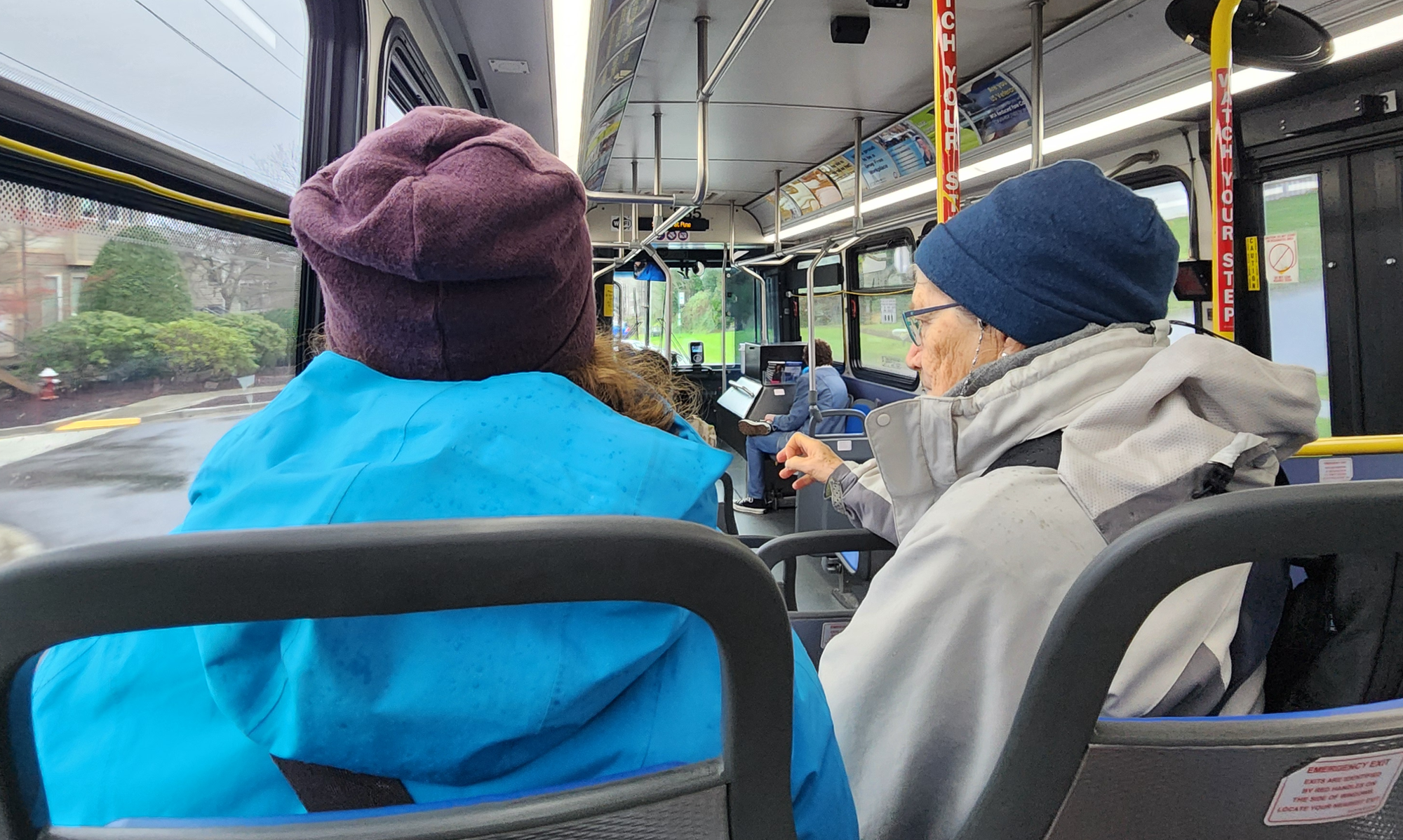 Two people sit in adjacent seats on a bus. 