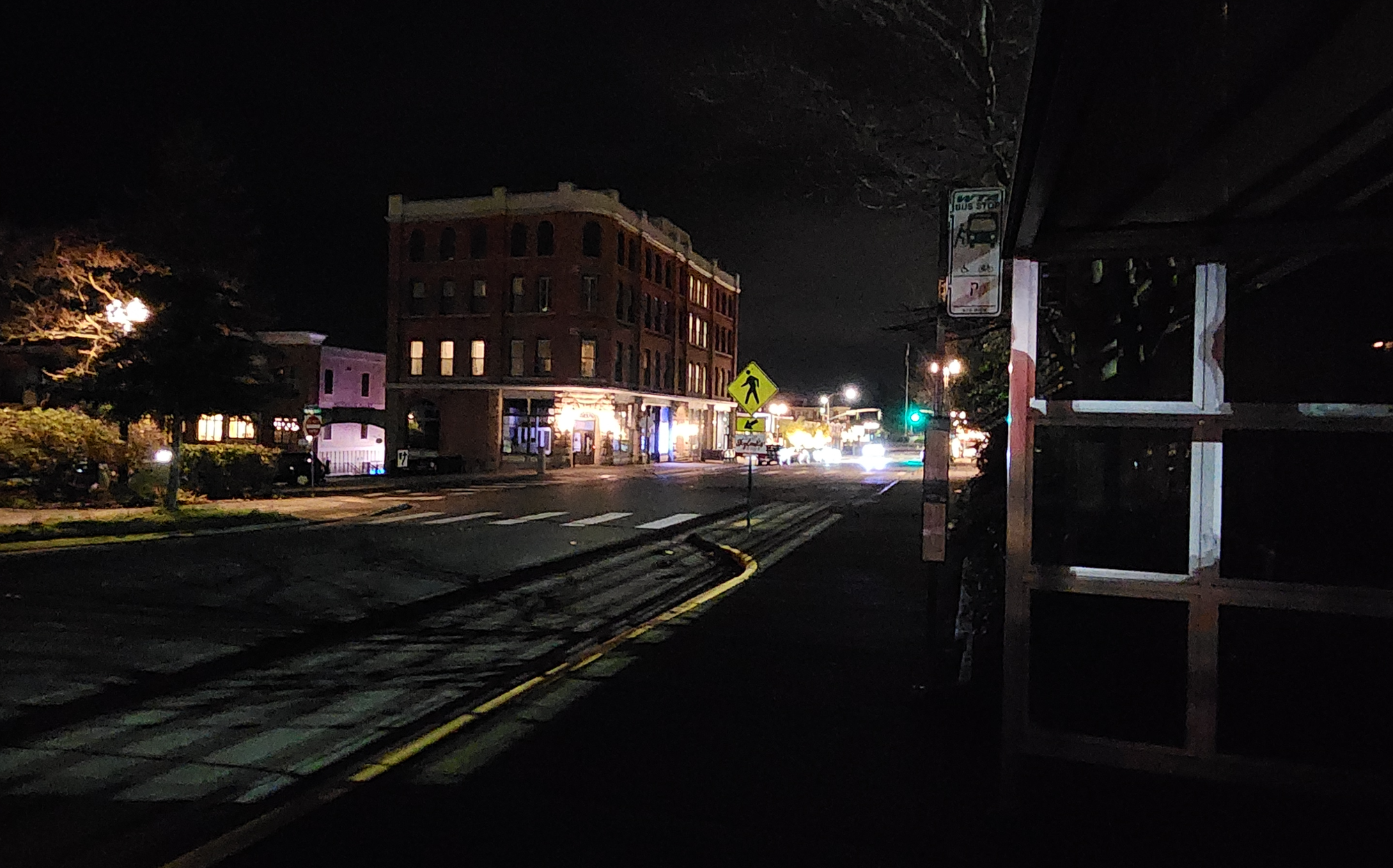 A nighttime view of 12th Street & McKenzie Avenue in Fairhaven, dimly lit crosswalk and the adjacent darkened WTA bus stop.