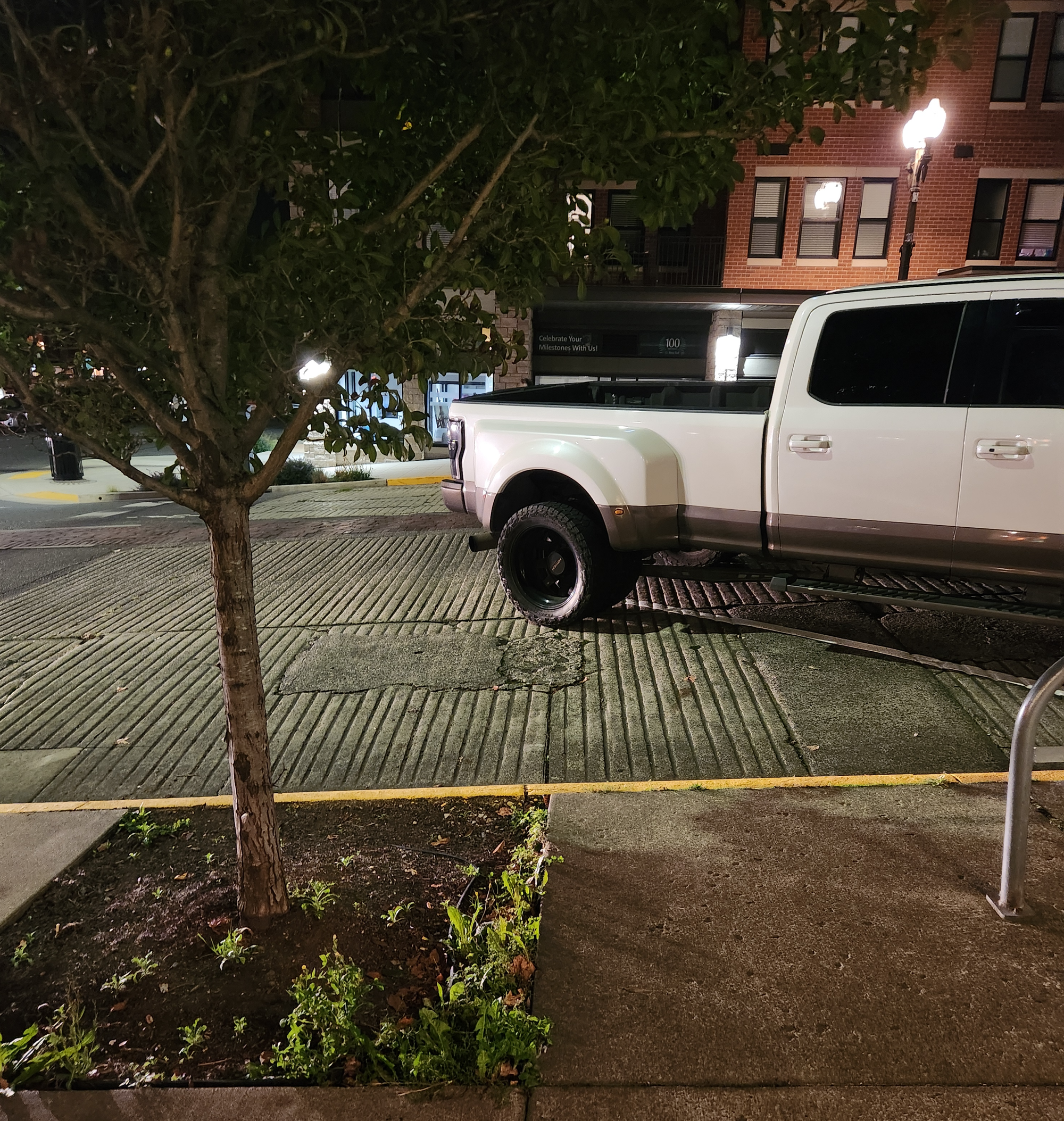 A large white pick-up truck doesn't fit in an angled parking space, jutting out into the street. 